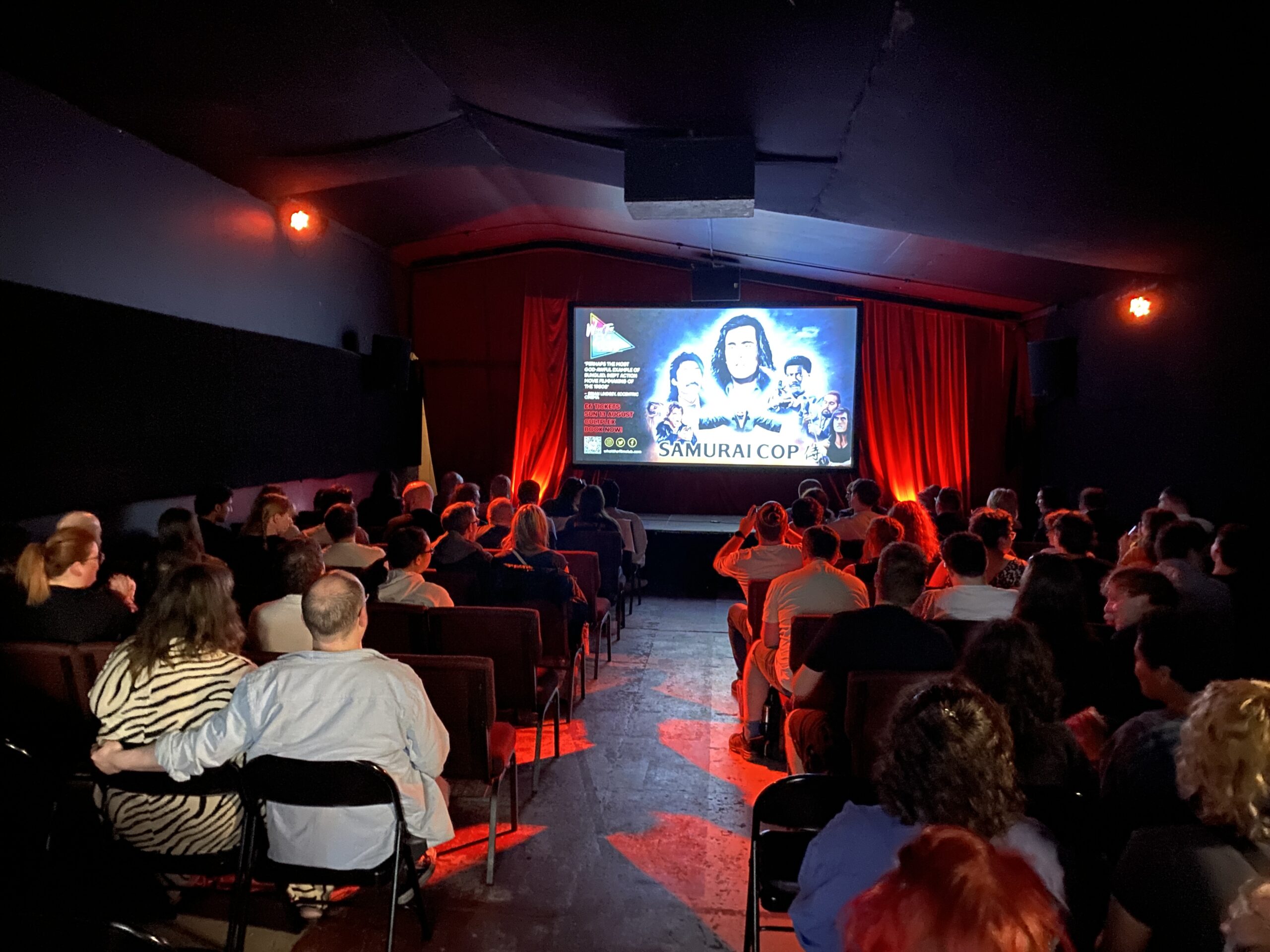 Cultplex - a cosy cinema, light with red light taken from behind the audience.